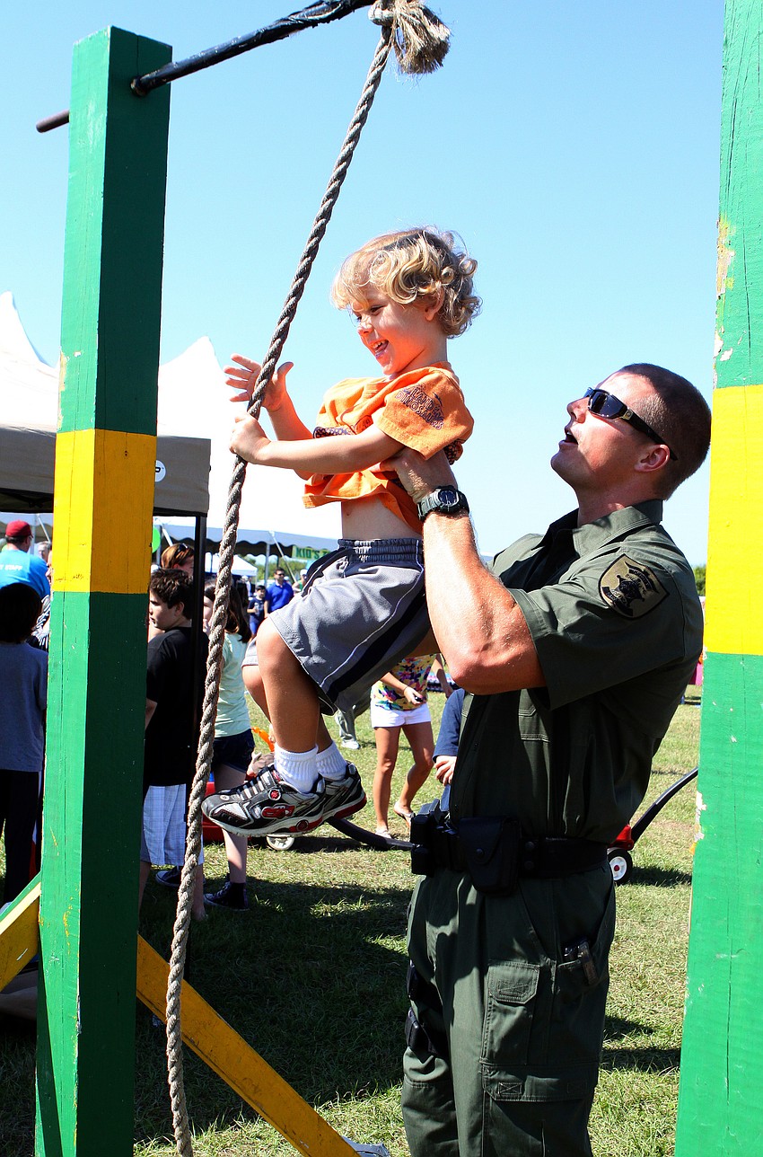 Stephen Collison of the Sarasota SWAT team helps Coltrane Marcusky, 3, climb up the rope at the SWAT obstacle course on Saturday, March 19 at the Sarasota Springfest out at Palmer Ranch.