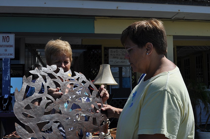 Carol Roberts holds a piece of decorative ironwork for Marcy Craddock's inspection.