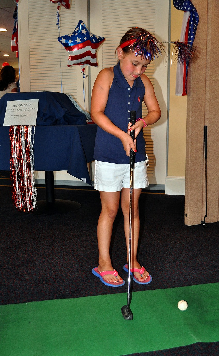 Aidyn Thompson, 6, tries to putt a golf ball into a hole at one of the many game stations set up Monday, July 4 at Bird Key Yacht Club.