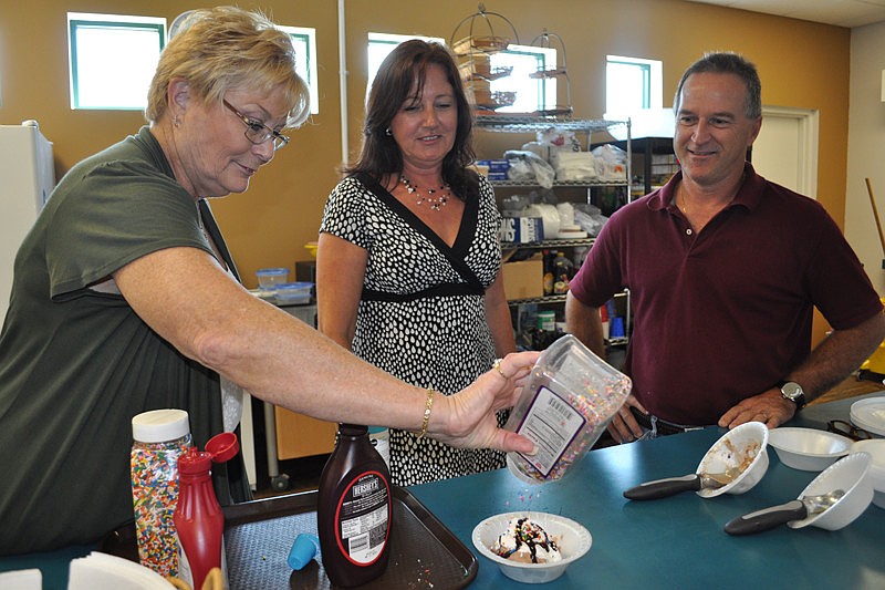 Volunteer Mary Anne McDevitt, left, builds an ice cream sundae for a guest. She is pictured with event coordinator Susan Myers and volunteer John Jackson.