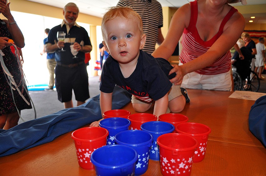 Matthew Crouch, 1, figures out a way to get a ping pong ball into a cup at one of the game stations set up Monday, July 4 at Bird Key Yacht Club.