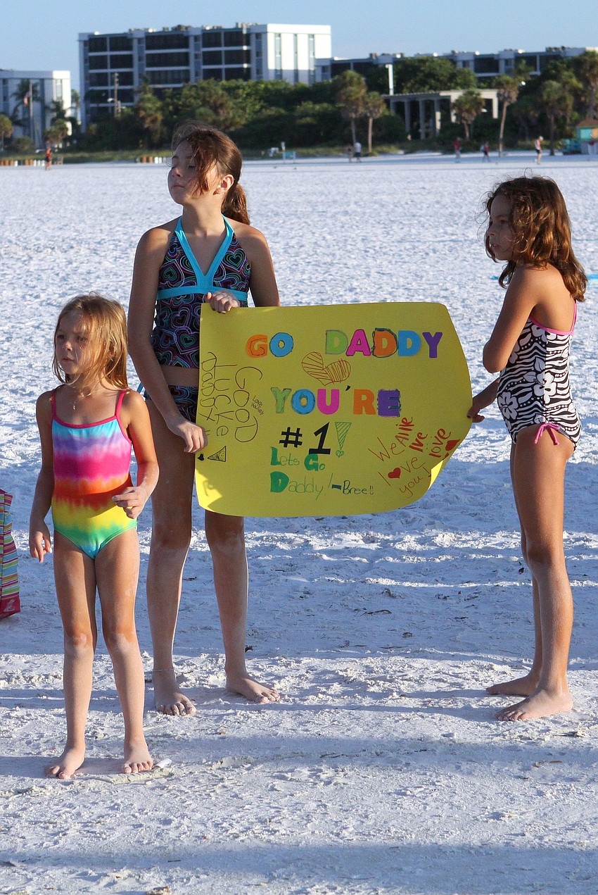 Bree, 10, and Hailey, 8, hold their homemade sign while their younger sister, Allie, 5, Vazquez keeps a look out for their dad, Yamani, Saturday, July 23 during the Siesta Key Triathlon out at Siesta Key Public Beach.