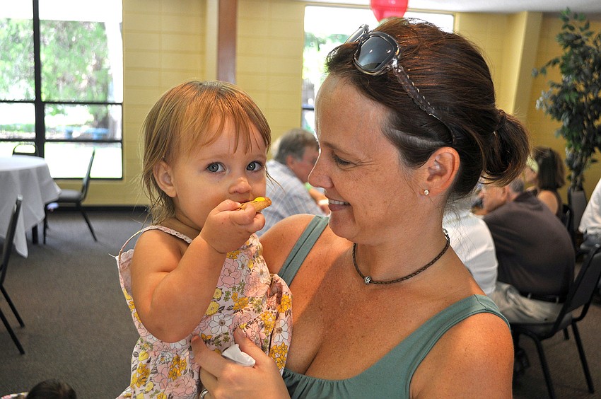 Sydney Soboleski, 1 Â½, enjoys eating an M&M cookie while being held by her mom, Sarah, Sunday, August 14 during the ice cream social in the Parish Hall at St. Boniface.