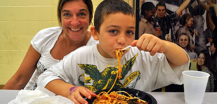 Leeland Berry, 8, chows down on some spaghetti while his mom, Laurie, smiles in the background during the CYD and Boys & Girls Club â€œFamily Dinner Nightâ€ Monday, Sept. 26, at the Lee Wetherington Boys & Girls Club.