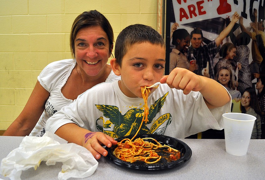 Leeland Berry, 8, chows down on some spaghetti while his mom, Laurie, smiles in the background during the CYD and Boys & Girls Club â€œFamily Dinner Nightâ€ Monday, Sept. 26, at the Lee Wetherington Boys & Girls Club.