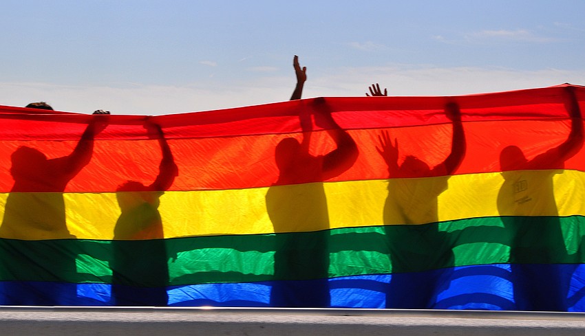 People wave at a helicopter flying overhead while they held up a mile-long rainbow flag Saturday, Oct. 1, on the Ringling Bridge.