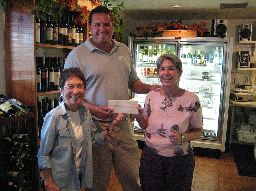 Susan Landau and Madelyn Spoll of the Garden Club get presented a check from Hal Christensen with Harry's Continental Kitchens for the wine tasting fundraiser.