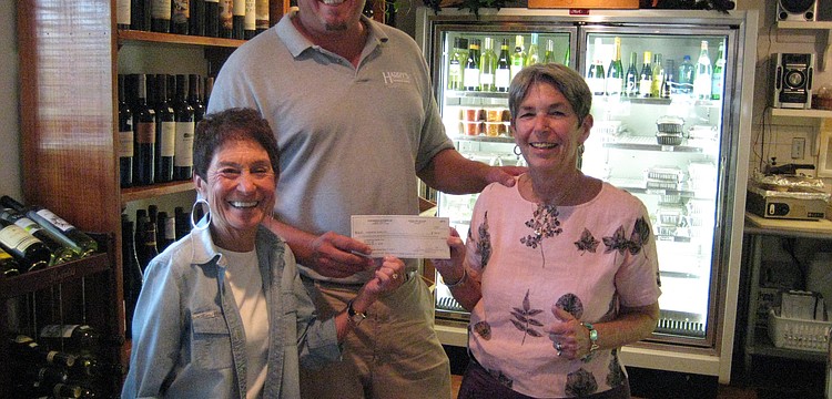 Susan Landau and Madelyn Spoll of the Garden Club get presented a check from Hal Christensen with Harry's Continental Kitchens for the wine tasting fundraiser.