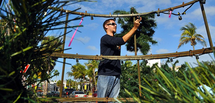Alex Morel, of Wagner Realty, stands up on one of the rings of the tree to hang up a branch.