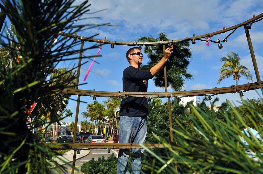 Alex Morel, of Wagner Realty, stands up on one of the rings of the tree to hang up a branch.