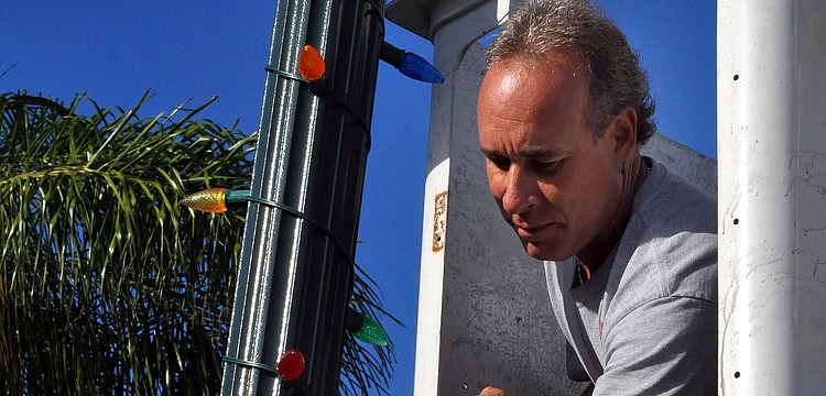 Steve Molinaro, of SJM Enterprises, works to put up and plug in colorful holiday lights on all the lamp posts, Saturday, Nov. 19, in Siesta Key Village.