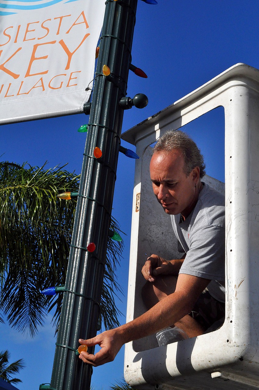 Steve Molinaro, of SJM Enterprises, works to put up and plug in colorful holiday lights on all the lamp posts, Saturday, Nov. 19, in Siesta Key Village.