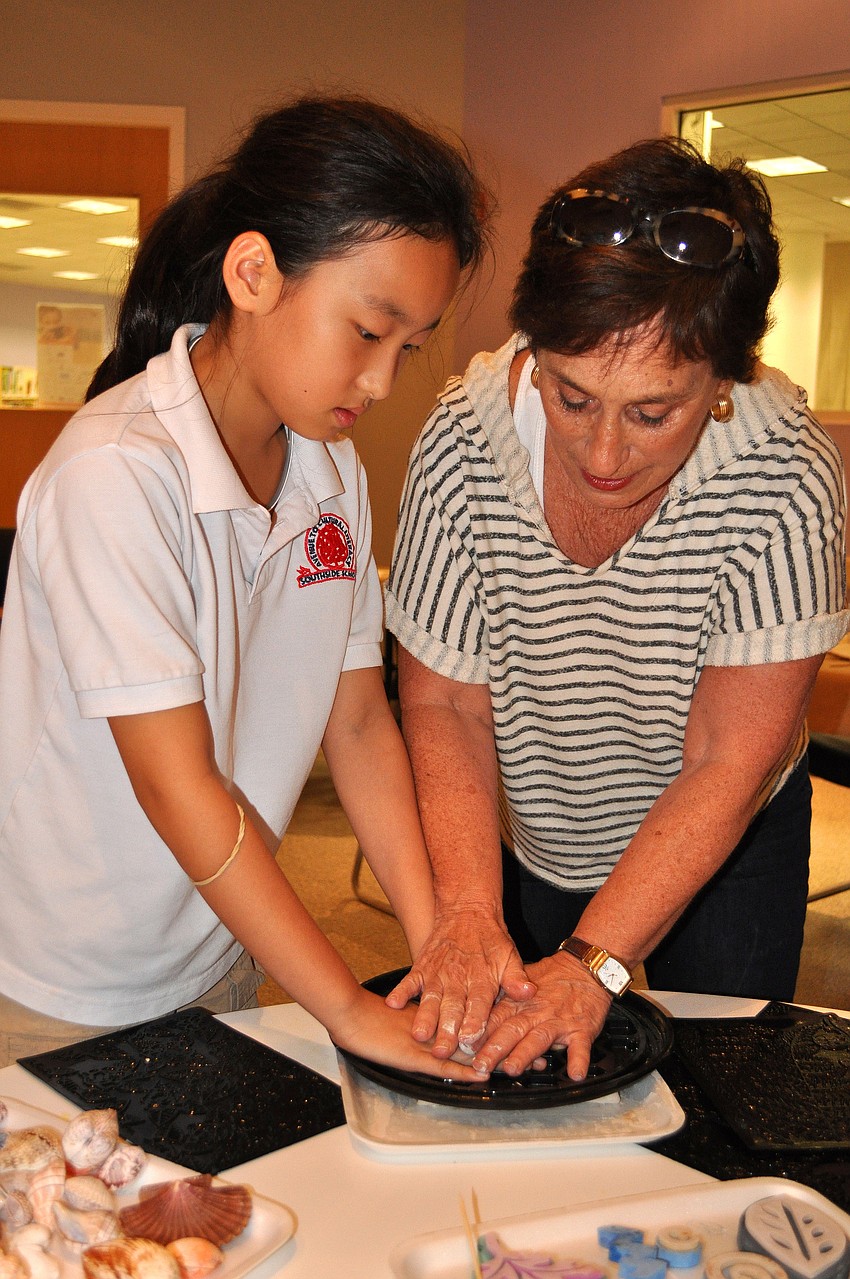 Judy Pirkey helps Bari Namgoong, 9, push down and create a background pattern on a clay slab.
