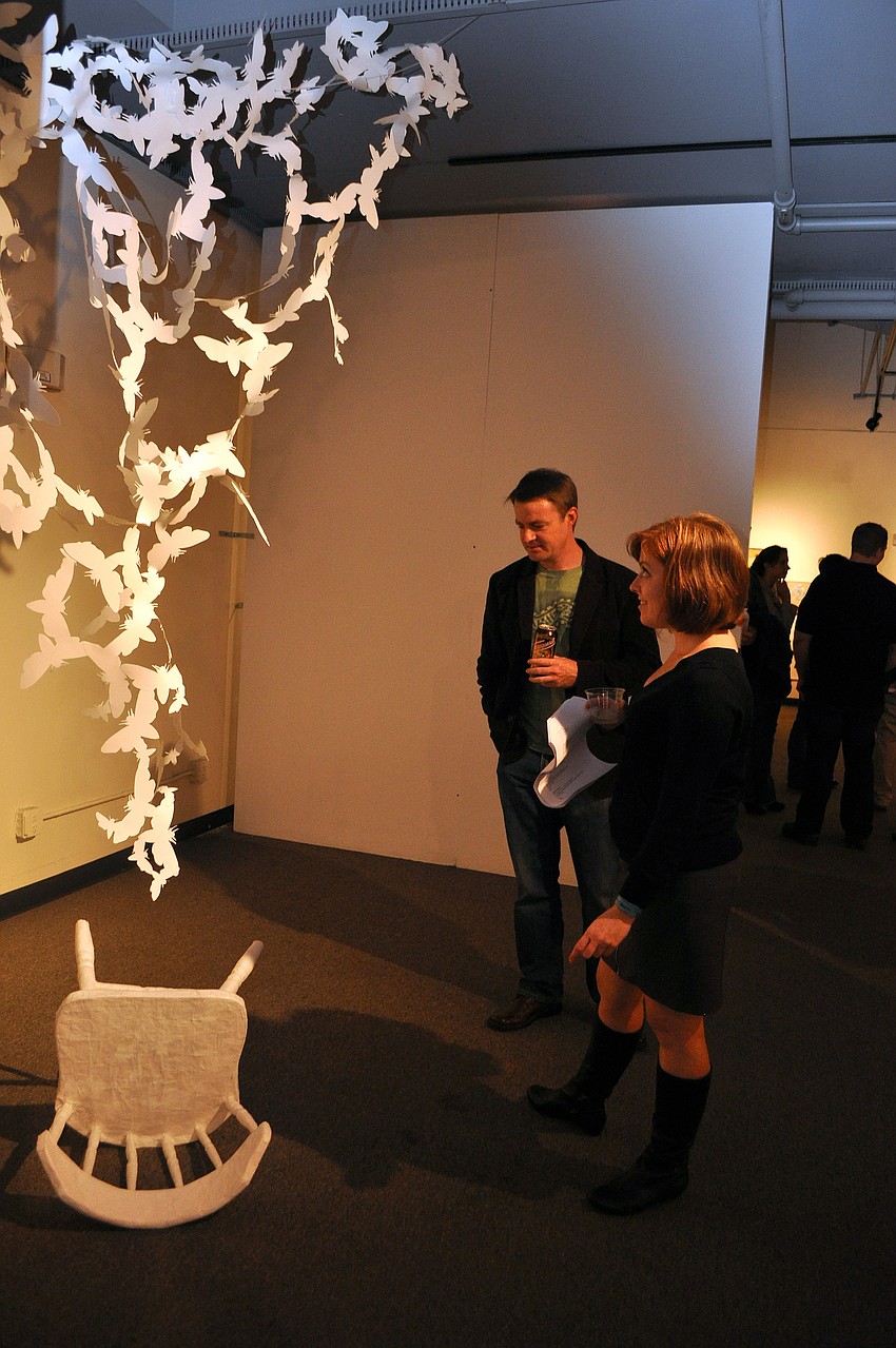 Sarah Kunkel and Glenn Darling check out a piece involving a chair and cut-out butterflies during the opening of THIRTEEN, Friday, Dec. 9, at G Wiz.