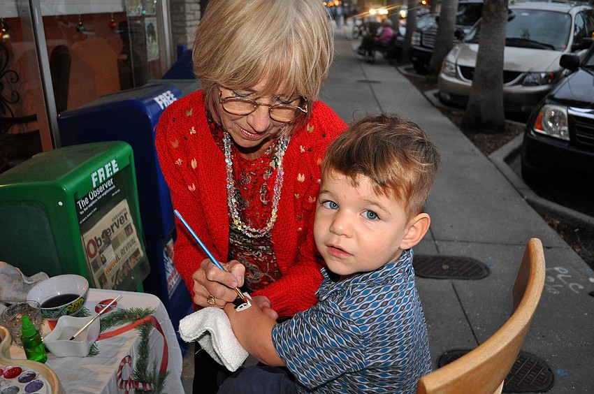 Diane Schmidt paints a snowman face on Andre Hersomâ€™s, 2, arm out in front of Rosebay Realty, Friday, November 9, during Southside Stroll.