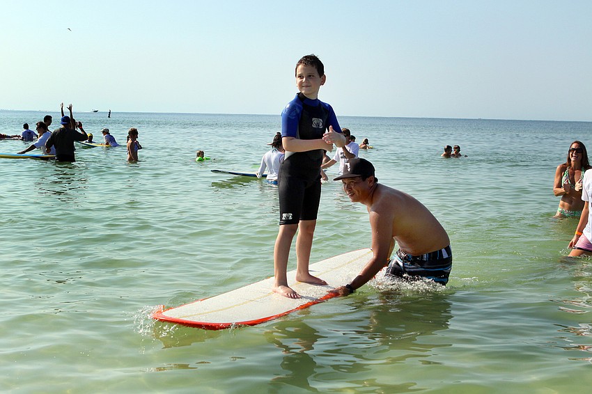 Blake Schlotthayer, 8, stands up and rides towards shore with the help of Chris Marquez Saturday, Sept. 17, during the Hang Ten for Autism surf event at the Siesta Key Public Beach.