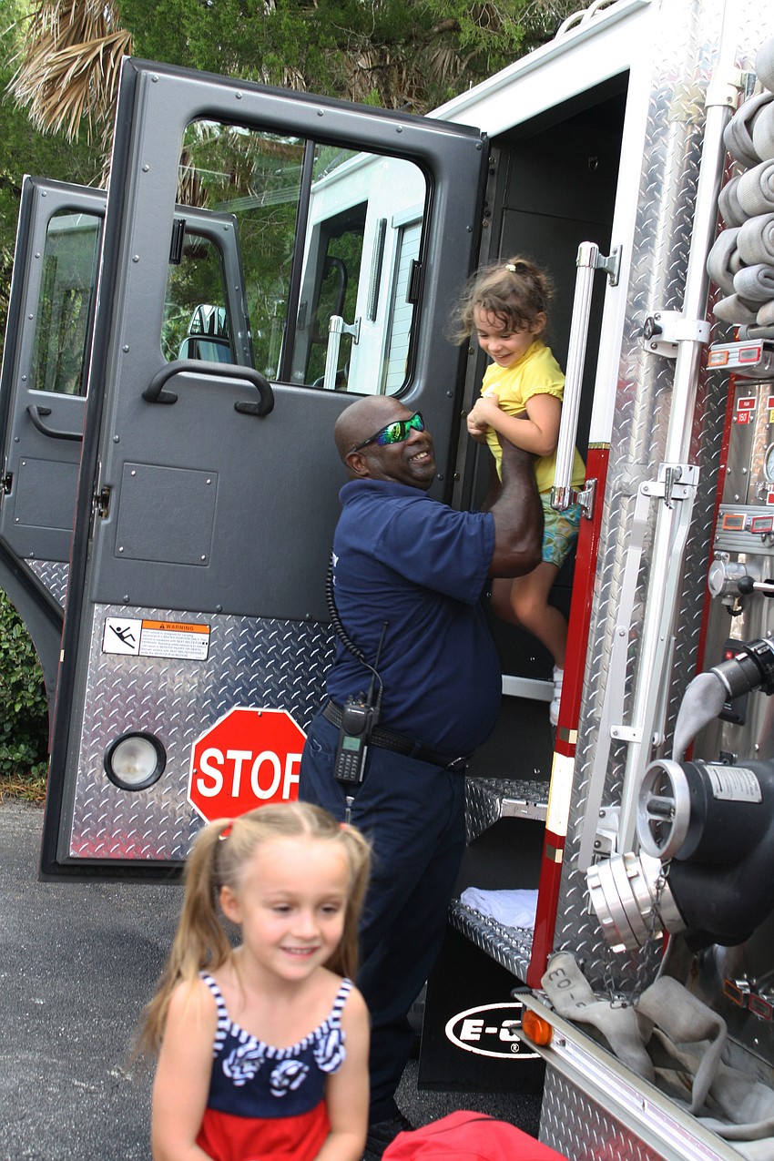 Violet Walsh Grins after taking a tour of the inside of the firetruck. Firefighter Ricky James hoists Giovanna Hansen out of the truck.