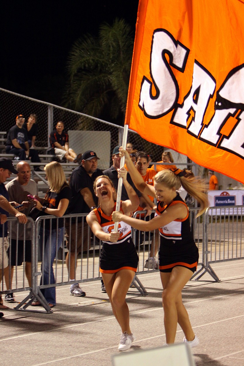 Two cheerleaders run down the track with a large Sarasota Sailors flag after the Sailors scored a touchdown.