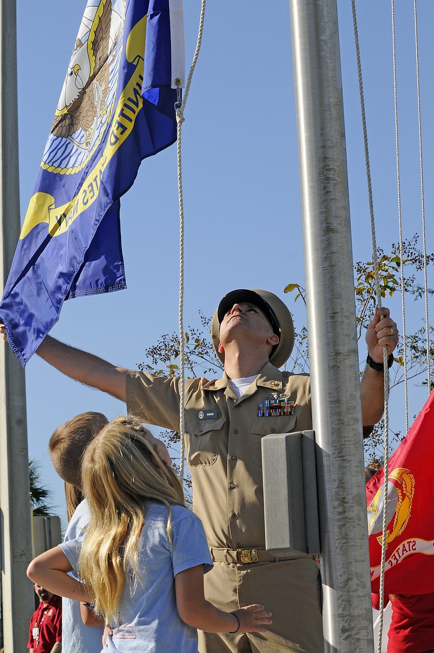 Third-graders Brady Greenamoyer and Rhien Forbes look on as Chief Petty Officer Troy Smith raises the Navy flag.