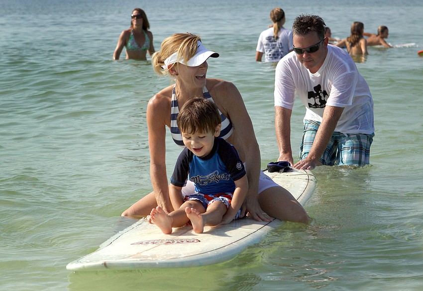 Lee Swain gives Jennifer Columbo and Ian Higgins, 3, a push on the surfboard.