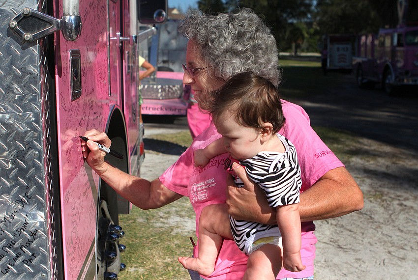 Kathy Benscoter signs a truck while holding her granddaughter, Laurel Harman, 14 mos.