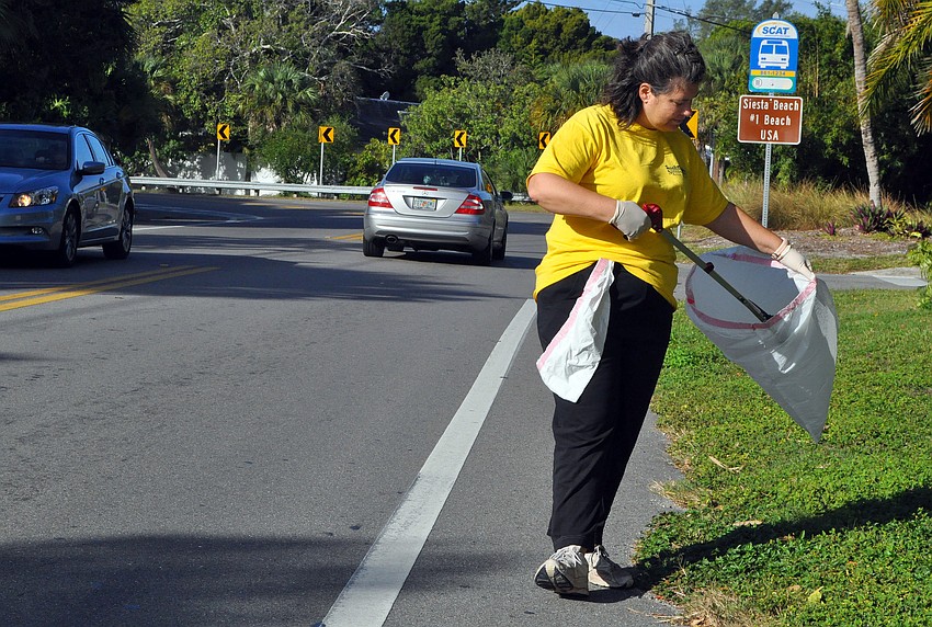 Maria Shay puts a piece of debris she found along Siesta Drive into her garbage bag.