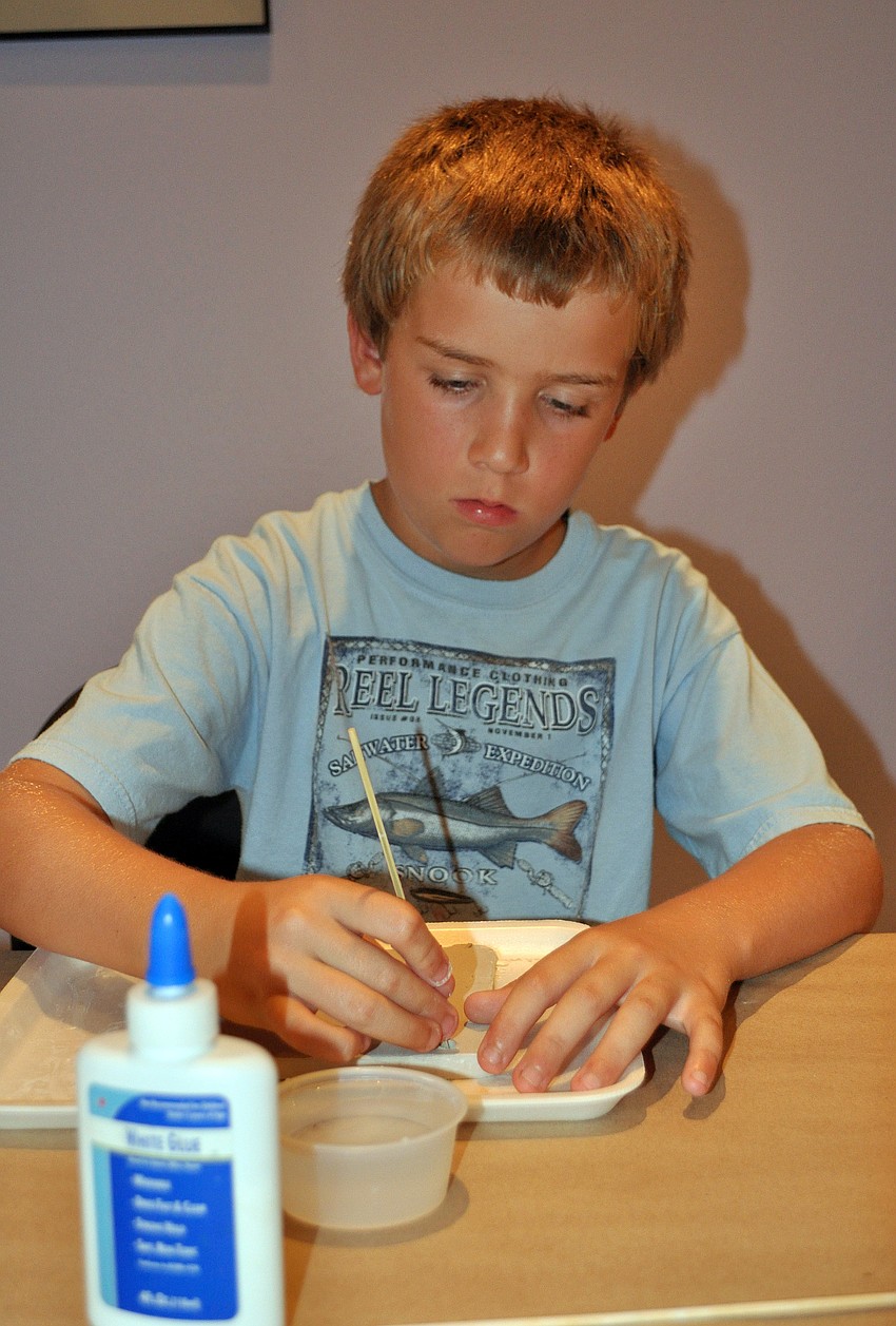 Ryan Murray, 9, creates one of the two holes in his plaque for the ribbon to go through so that it can hang on a wall.