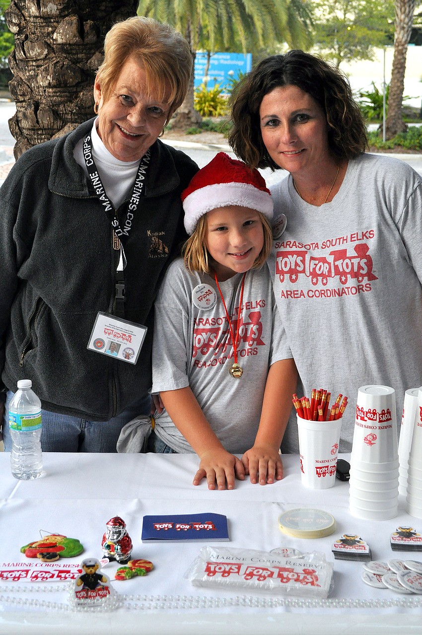 Sandy Lacey, Thealy Govaars, 9, and Cathy Govaars pose together while working the Toys For Tots table, Friday, November 9, during Southside Stroll.