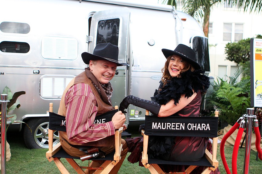 Dr. Larry Thompson and his wife, Pat, pose in movie star chairs labeled â€œJohn Wayneâ€ and â€œMaureen Oâ€™Haraâ€.