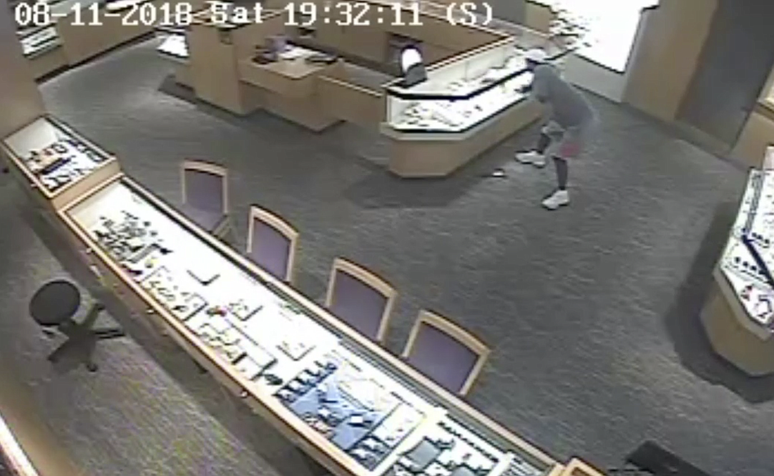 A robber pulls gold necklaces out of a display case at Kays Jewelry in Town Center. (Image courtesy of the FCSO)