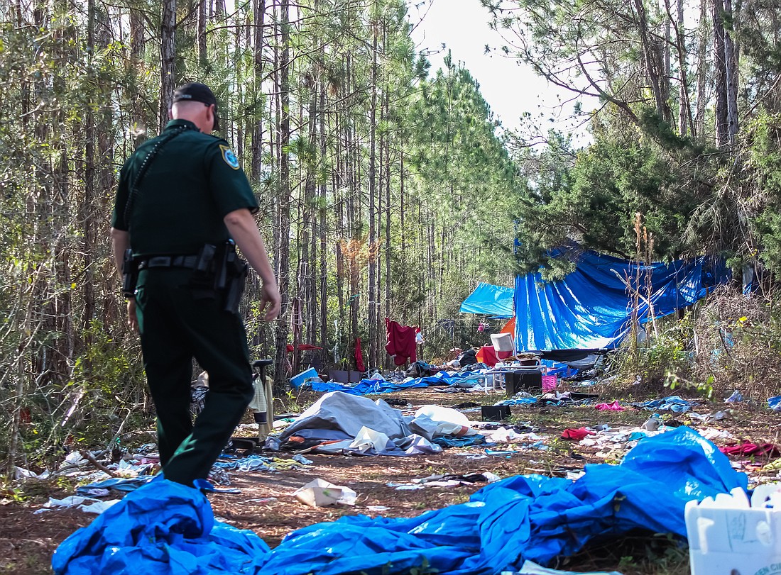 A Flagler County Sheriff's deputy walks through the pile of trash in the homeless camp in the woods behind the Flagler County Public Library. Photo by Ray Boone