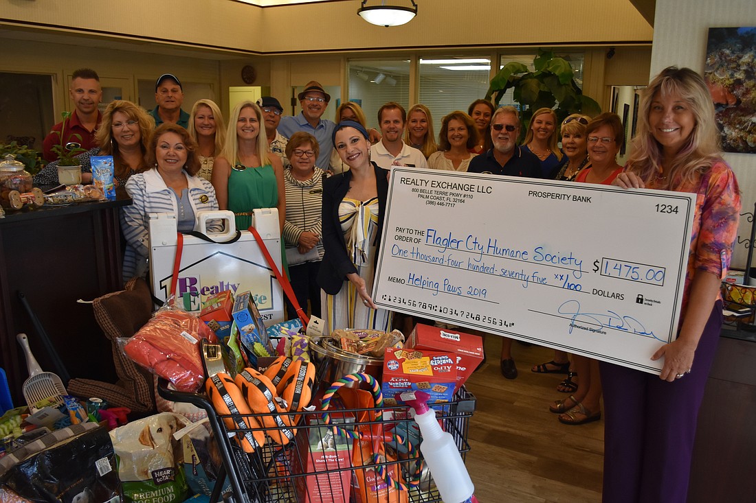 Flagler Humane Society Executive Director Amy Wade-Carotenuto holds the check from Realty Exchange LLC, in front of even more donated goods. Photo courtesy of Realty Exchange LLC