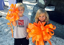 Jason Flovig, 4, and Isabella Balje, 3, held up two of the orange bows that were adorned on the new playground items at Forty Carrots.