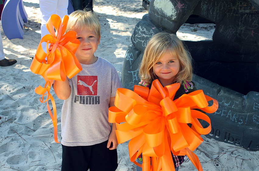 Jason Flovig, 4, and Isabella Balje, 3, held up two of the orange bows that were adorned on the new playground items at Forty Carrots.