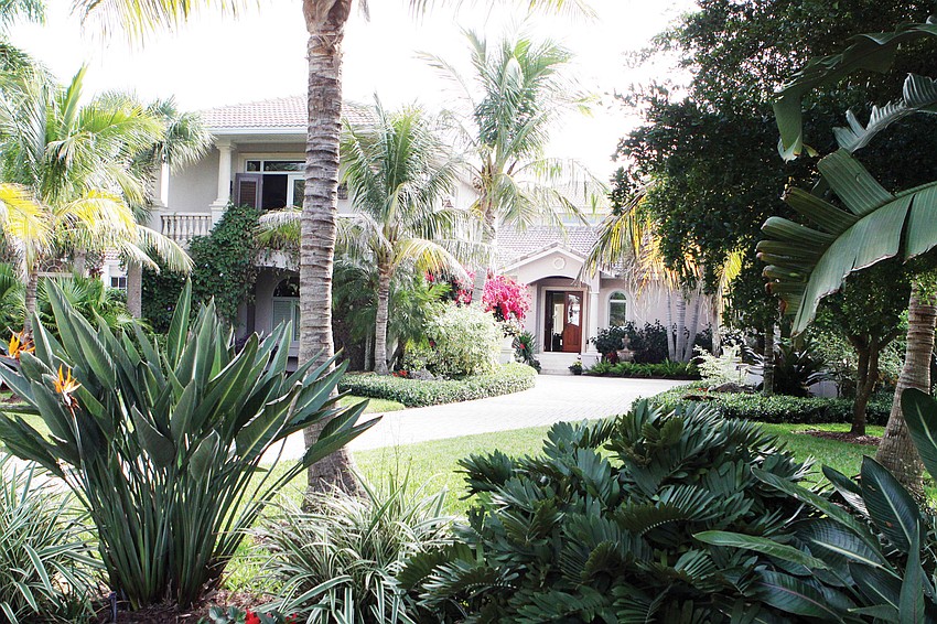 The home is set back from the road and has many plants and trees lining the driveway.
