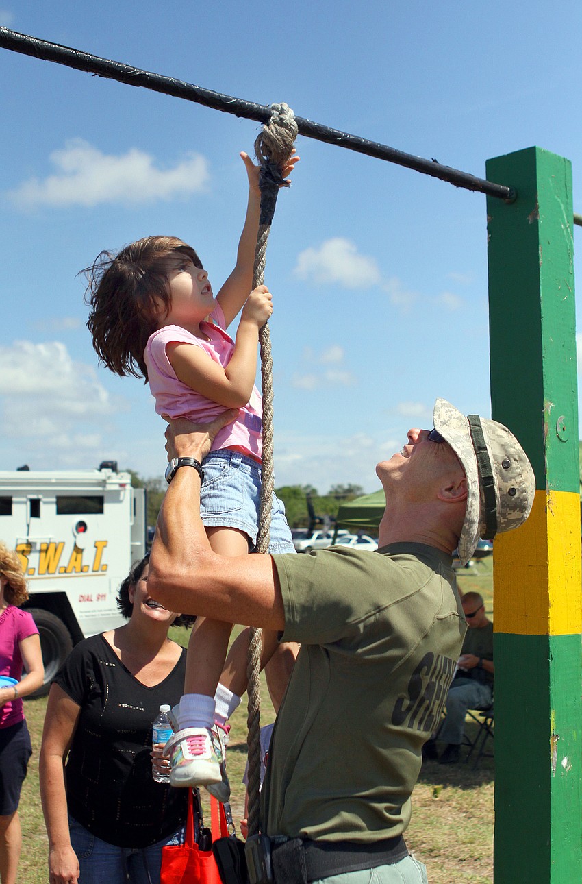 Ava DiRocco, 3, has some help from officer Shawn Johnson climbing up the rope at the obstacle course.