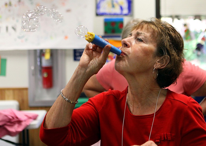 Janice Frankel blows bubbles as the children, parents and caregivers clean up the toys that were used during playtime.