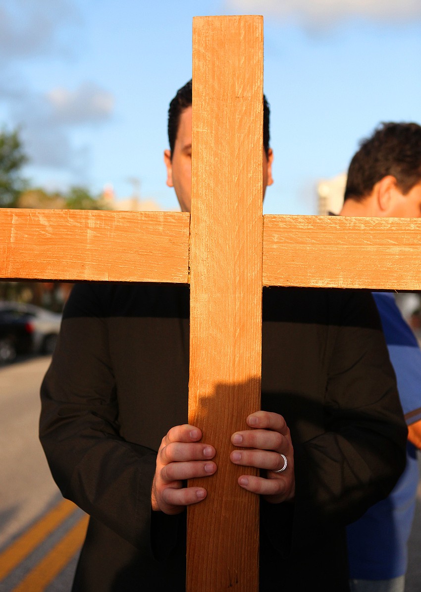Youth Director Christian Wood held the cross throughout the Stations of the Cross walk, Friday, April 6, on Main Street.
