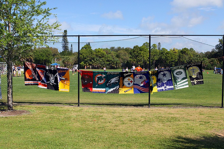 The flags of the different NFL teams that are represented out on the field by the NFL flag football teams hang on the side of one of the gates out at Glebe Park.