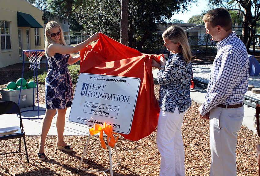 Ariane Dart and Ellen Steinwachs unveil the playground renovation sign as Jeff Steinwachs looks on, Tuesday, Jan. 24, at Forty Carrots.