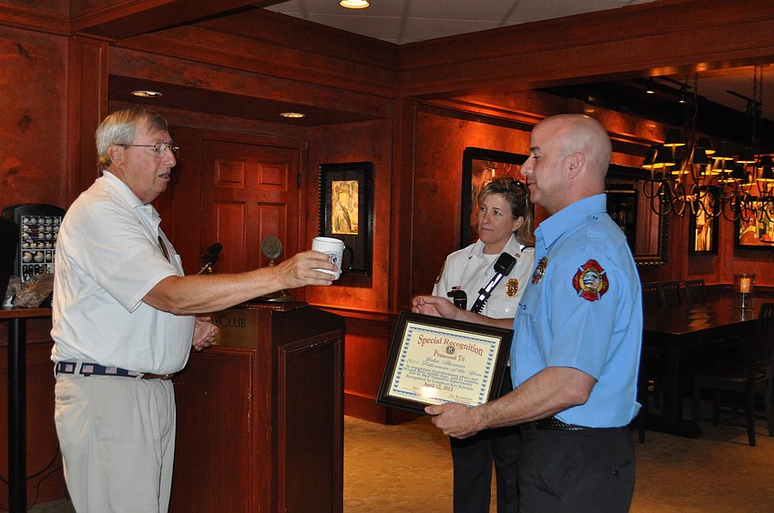 President John Wild presents a certificate and coffee mug to Firefighter Jim Reynolds, with Dep. Chief Sandi Drake standing by.