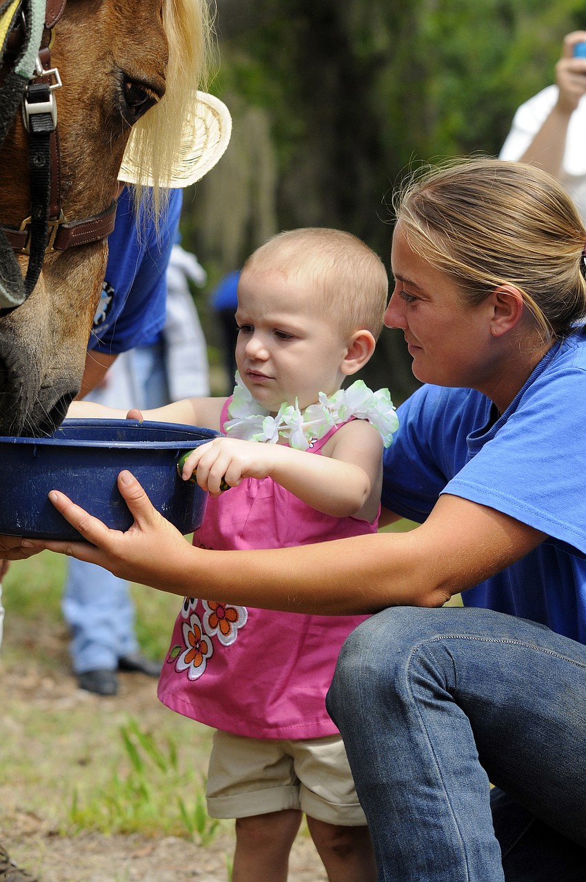 Two-and-one-half-year-old Izzy Dean helps Alissa Fabian feed one of the horses.