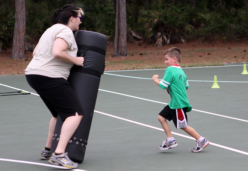 Lindsay Cornell prepares for Alex Hefti, 5 Â½, to run into the bag with a football at one of the many obstacle courses set up out on the basketball courts during Healthy Kids Day, Friday, April 20.