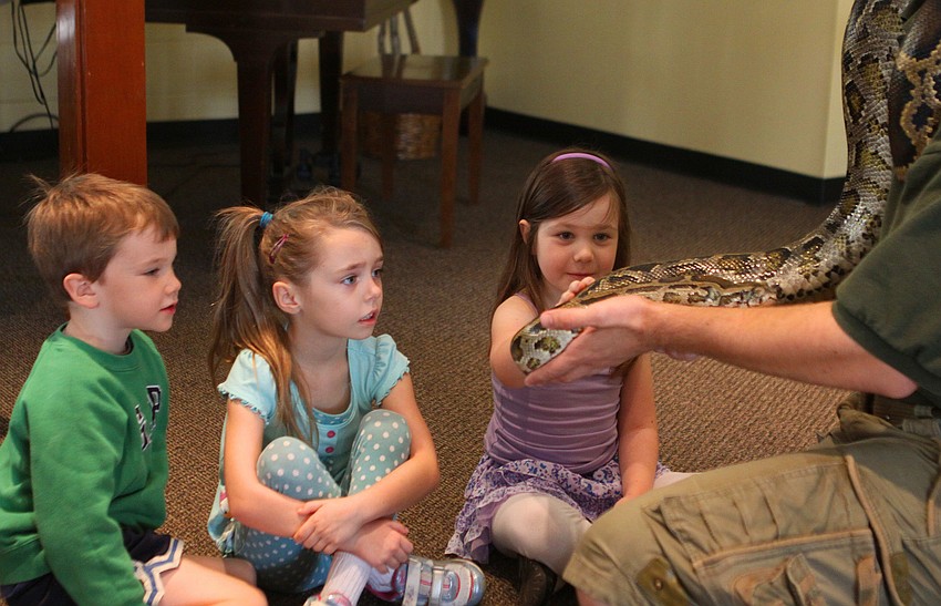 Madilyn Hagney touches Lucky, a Burmese python, as Chance McCarter and Linda Hayes wait their turn, Thursday, Jan. 12, inside the Parish Hall at St. Boniface.
