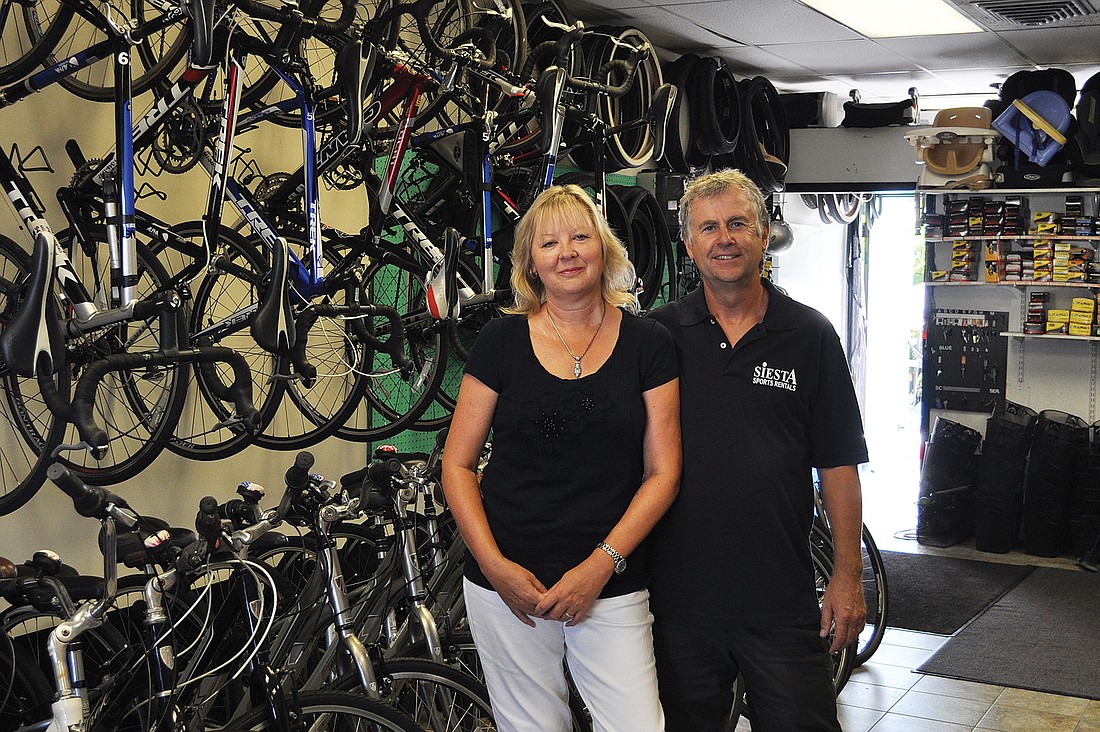 Sheila and Mike Lewis stand under the towering wall of bicycles the couple rents out as owners of Siesta Sports Rentals.