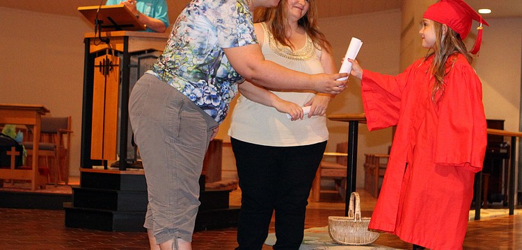 Violet Walsh, 5, receives her diploma from her teachers Connie Graham and Kat Wors as Dick Aubry looks on, Friday, June 1, at St. Boniface.