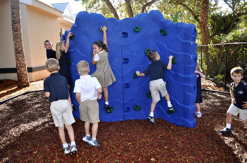Some of the younger students try climbing up the smaller rock wall on the playground.