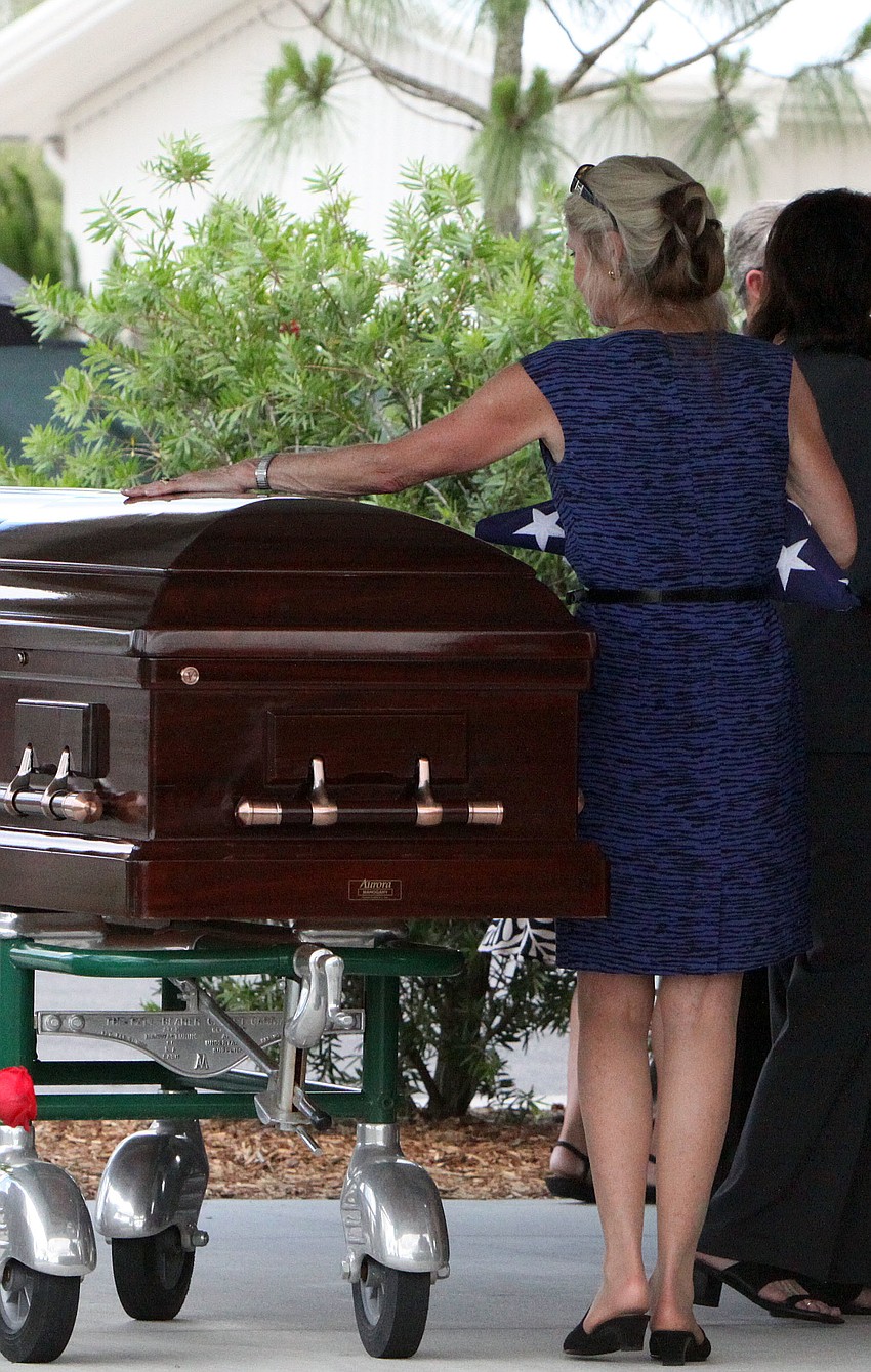 Leslie Hogle runs her hand along her husbandâ€™s casket following the burial ceremony.
