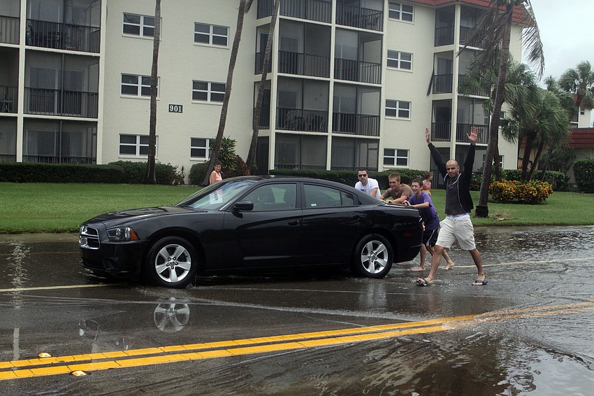 A group of guys push their car through the last bit of Beach Road where it was flooded after getting stuck in the water.