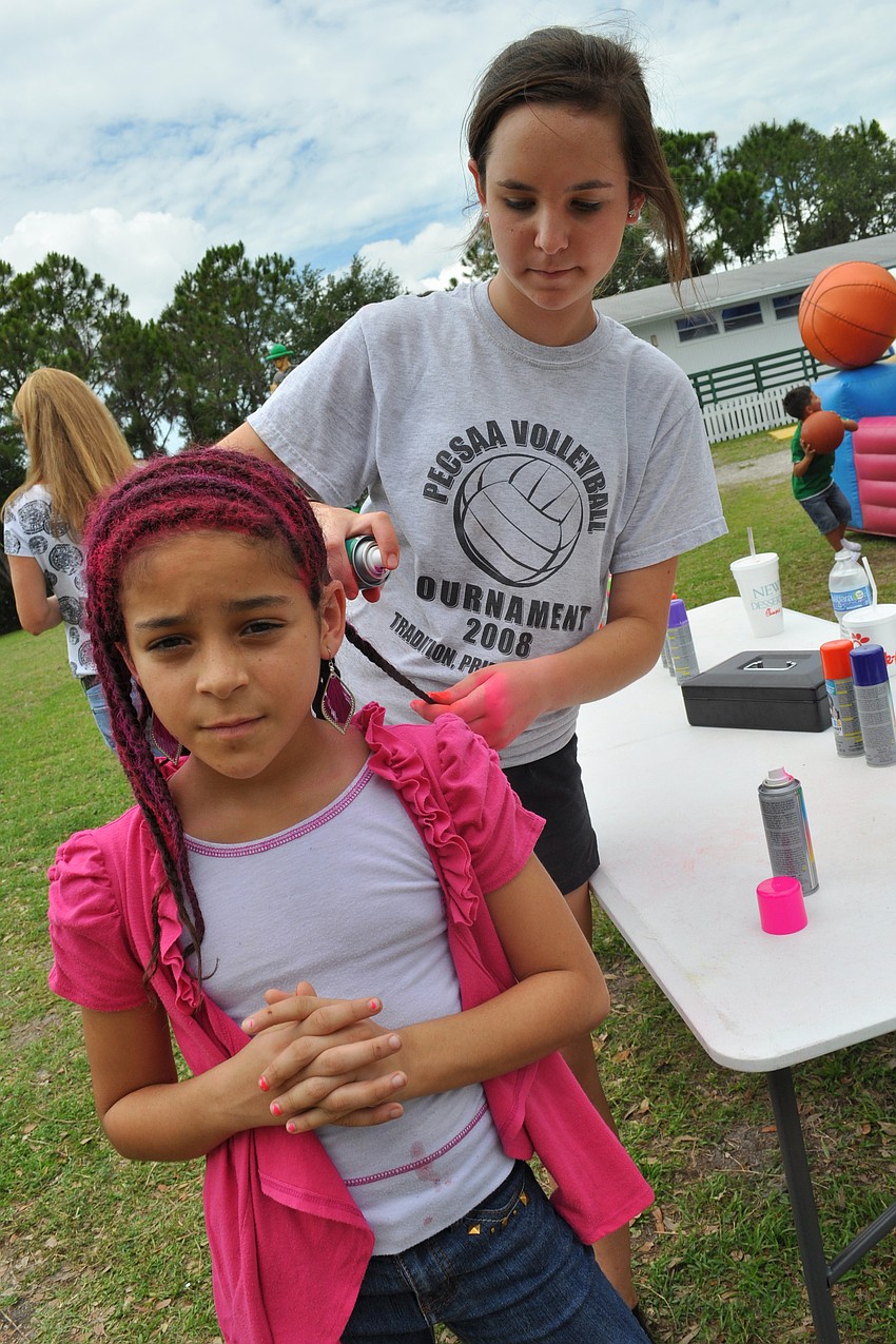 Alyencia Mendez, 9, gets her hair spray-painted pink and purple by volunteer Nicole Haluska, of Braden River Middle School.